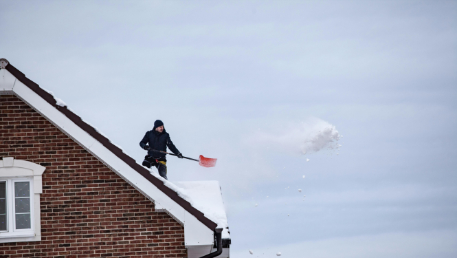 Vīrietis šķūrē sniegu nost no jumta.