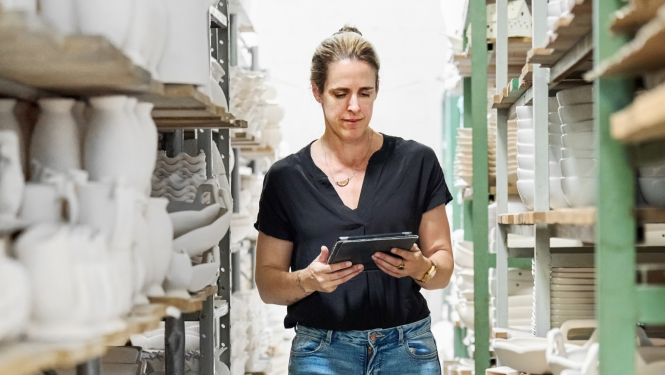 Cilvēks trauku noliktavā ar planšeti rokās.